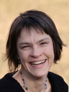 Julia Meyer lacht herzlich, mit dunklem Haar vor neutralem Hintergrund.